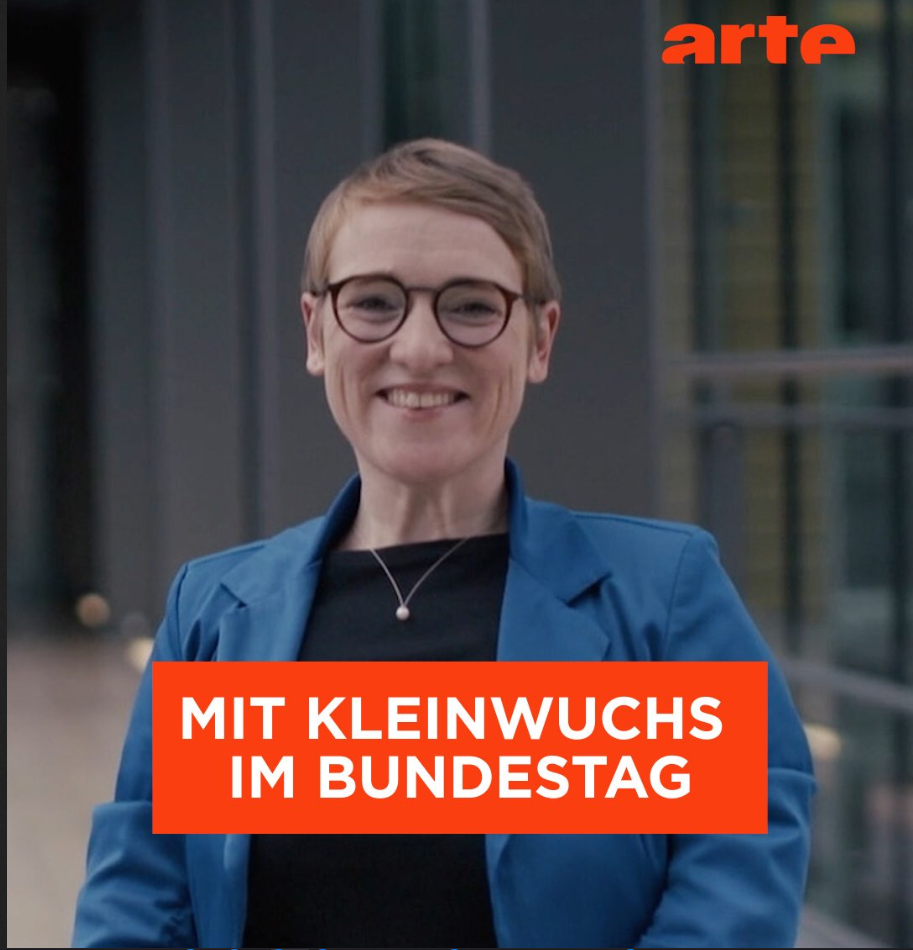 Person: Simone Fischer, lachend in einem Gang. Text: "Mit Kleinwuchs im Bundestag"