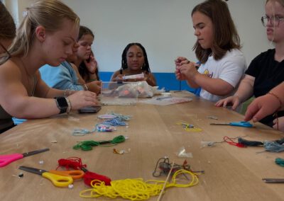 Gruppe von Personen sitzt an einem Tisch mit bunten Garnen, Scheren und Perlen und arbeitet an Bastelprojekten