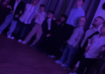 Kinder singen zusammen mit den Schultern beisammen und schaukeln bei einer Veranstaltung mit violetter Beleuchtung.