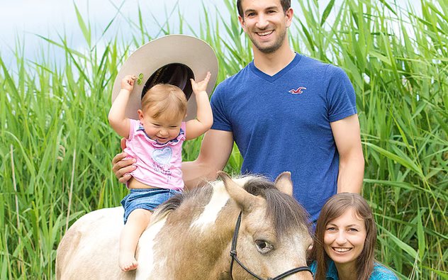 Drei lächelnde Personen mit einem Kind auf einem Pony auf einer Wiese