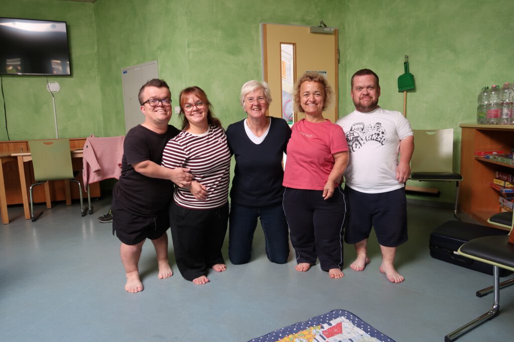 Gruppe von 5 Personen stehen Barfuß nebeneinander und lächeln in die Kamera.